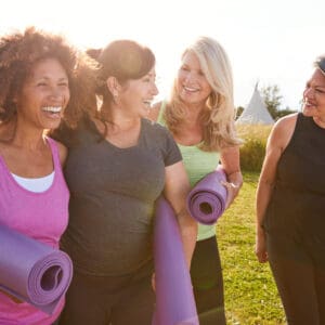 Group of middle-aged women outdoors holding yoga mats and smiling together before or after exercise.