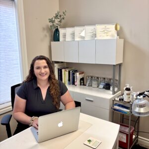 Dr. Ceilidh Flanagan, ND smiling at her desk in a treatment room at Hudson Integrative Healthcare in Stoney Creek.