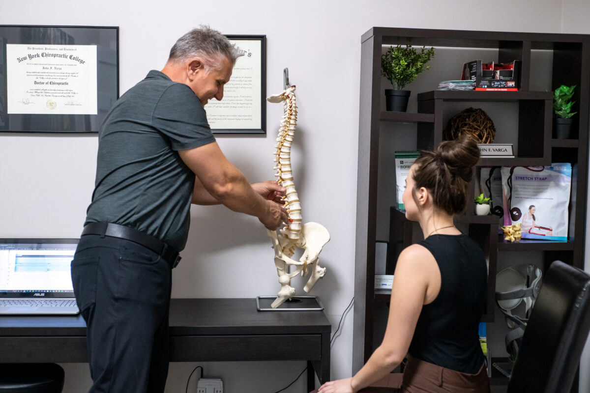 Chiropractor explaining spinal alignment and posture using a spine model during a patient appointment