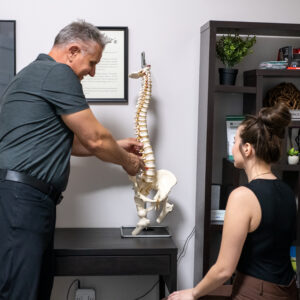 Chiropractor explaining spinal alignment and posture using a spine model during a patient appointment