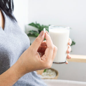Woman holding a supplement tablet with a glass of milk, representing nutritional supplements used as part of an individualized cholesterol and cardiovascular health plan.