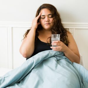 Woman experiencing fatigue and headache while resting in bed, symptoms that can be associated with hypothyroidism.