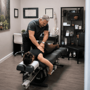 Chiropractor performing a lower back adjustment on a patient lying face down on a chiropractic treatment table in a clinic.