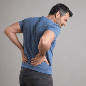 Man standing with both hands on his lower back and a facial expression of pain, illustrating acute or persistent lower back discomfort.