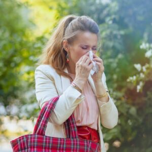 Woman outdoors blowing her nose with a tissue during cold and flu season.